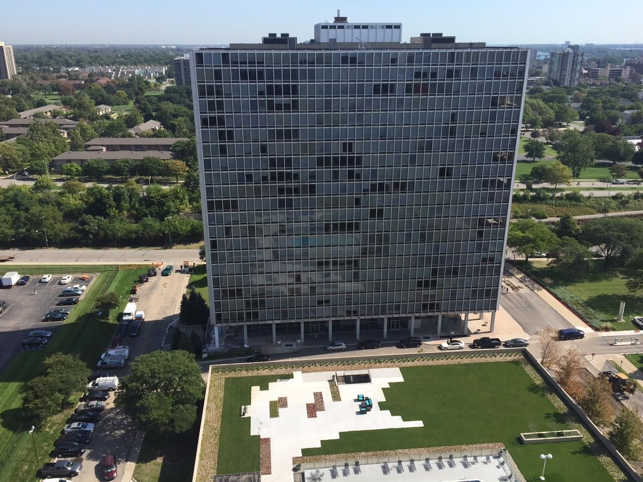 Aerial view of a tall glass office building with a green lawn and white courtyard in front.