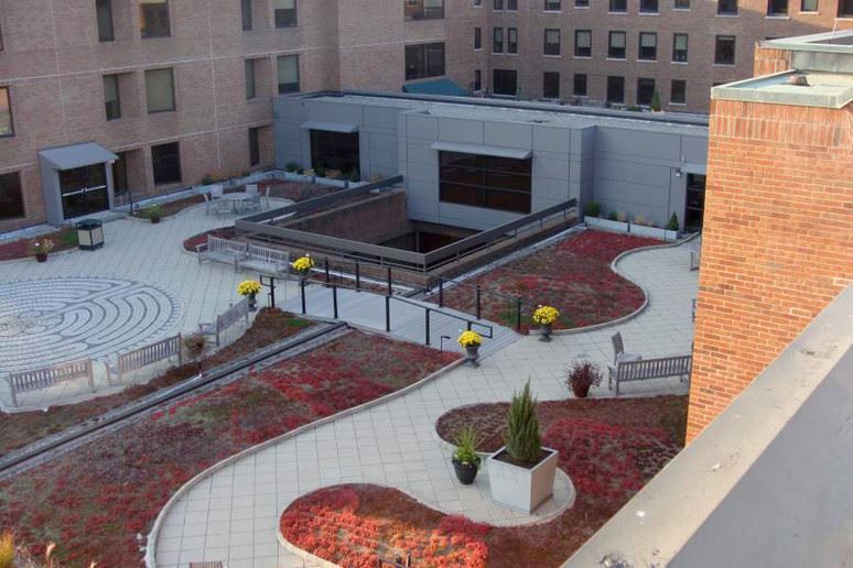 Rooftop courtyard with red planters, benches, and walkways beside brick buildings