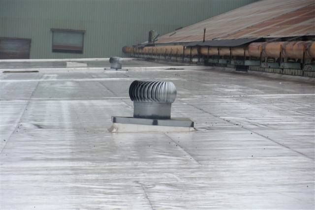 Rooftop ventilation fan centered on a flat, wet-looking white roof beside a long building wall