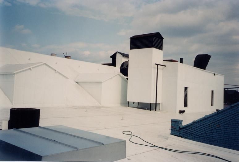 White industrial rooftop with vents, chimneys, and a blue roof edge under a cloudy sky