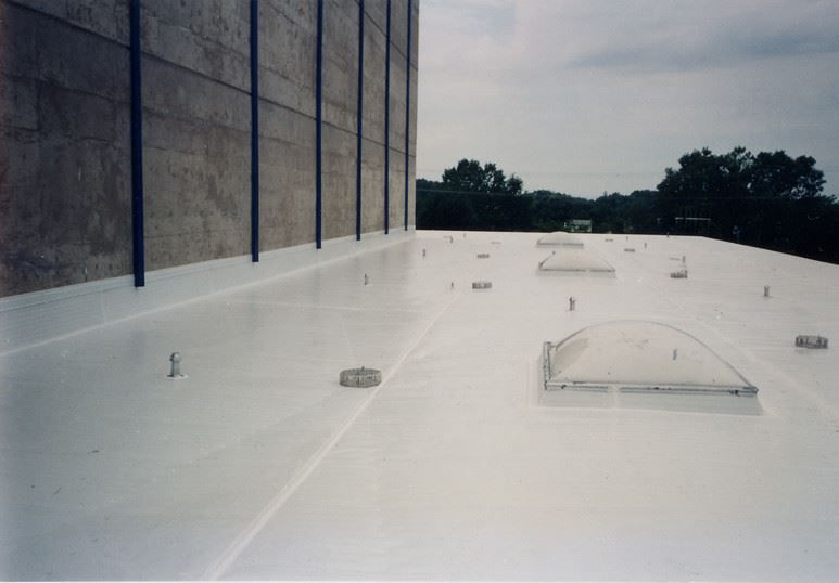 White rooftop with vents beside a tall brick building and trees in the distance