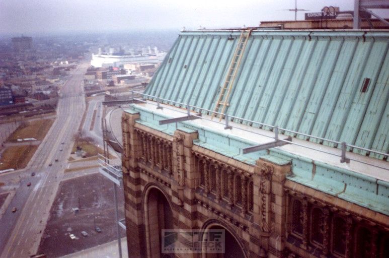 Rooftop view of a historic building with a green copper roof overlooking a city street and river.