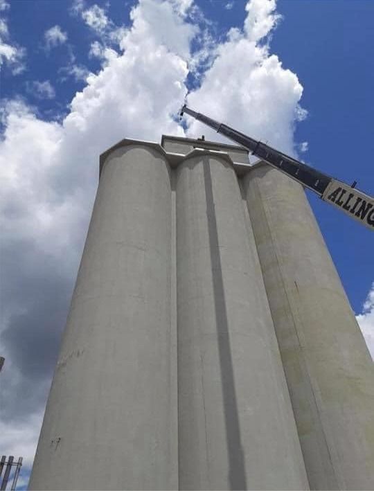 Tall concrete grain silos against a blue sky, with a raised conveyor arm overhead