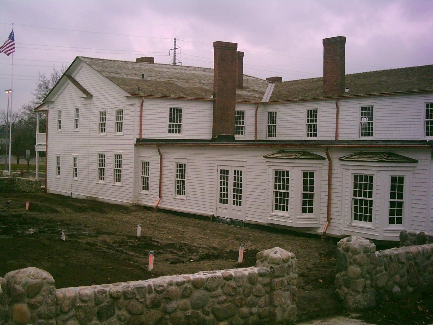 White historic building with chimneys and many windows, viewed from a stone wall on an overcast day