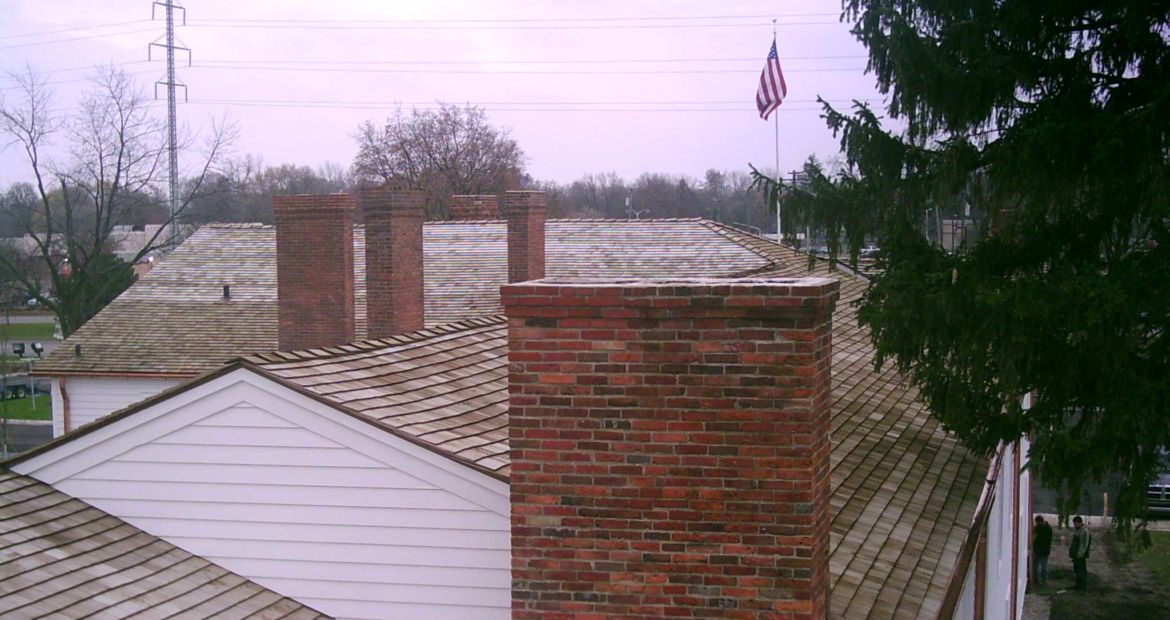Rooftops with brick chimneys and bare trees under an overcast sky.
