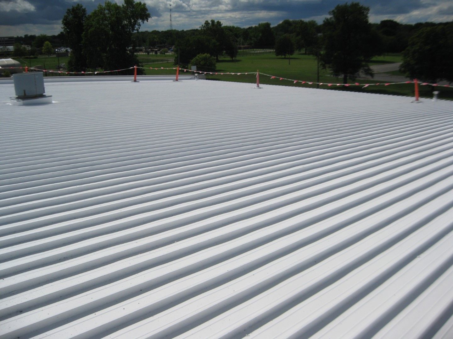 White ribbed rooftop with several orange safety posts under a cloudy sky