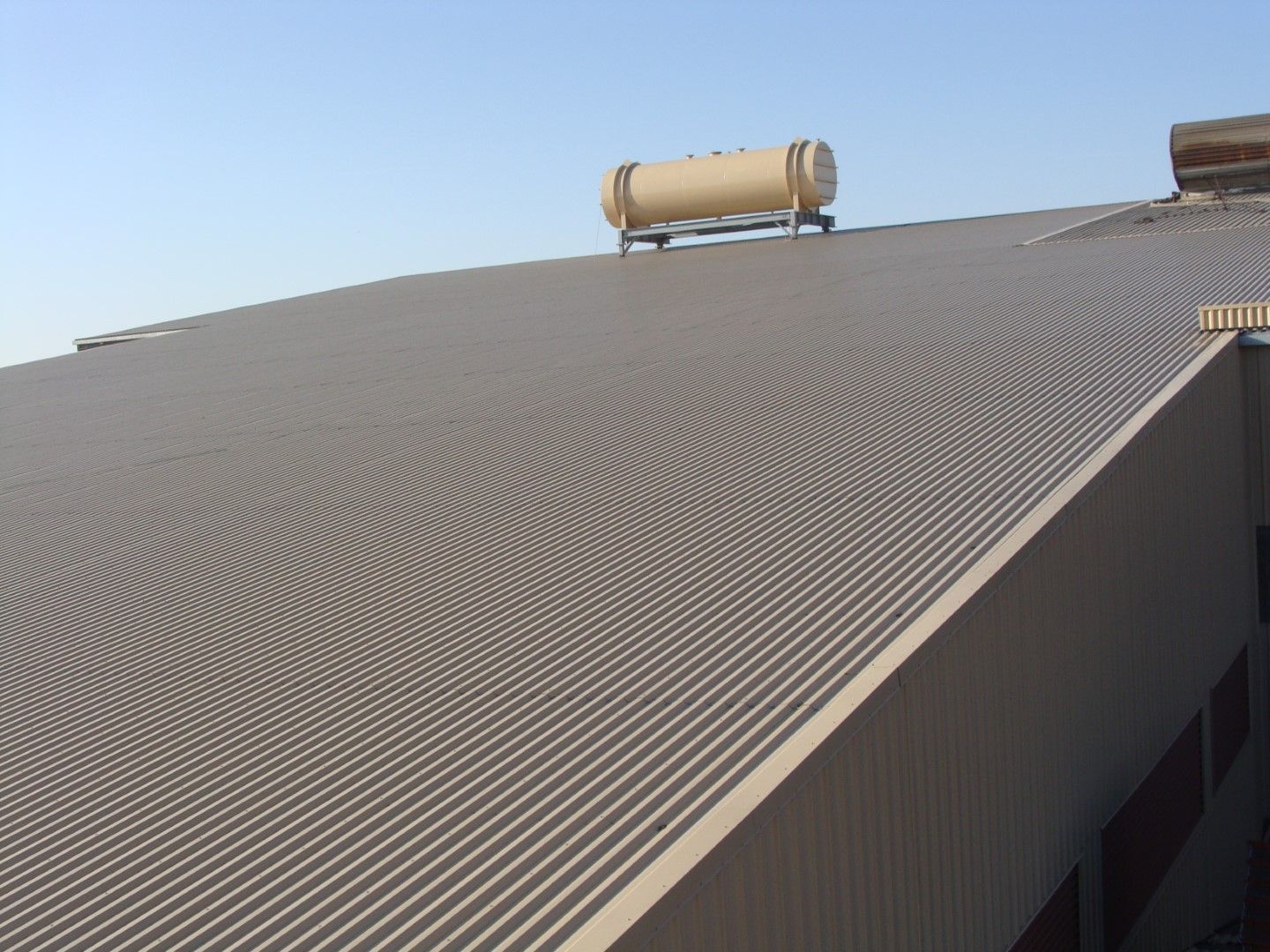 Corrugated metal roof with a cylindrical tank near the ridge under a clear blue sky