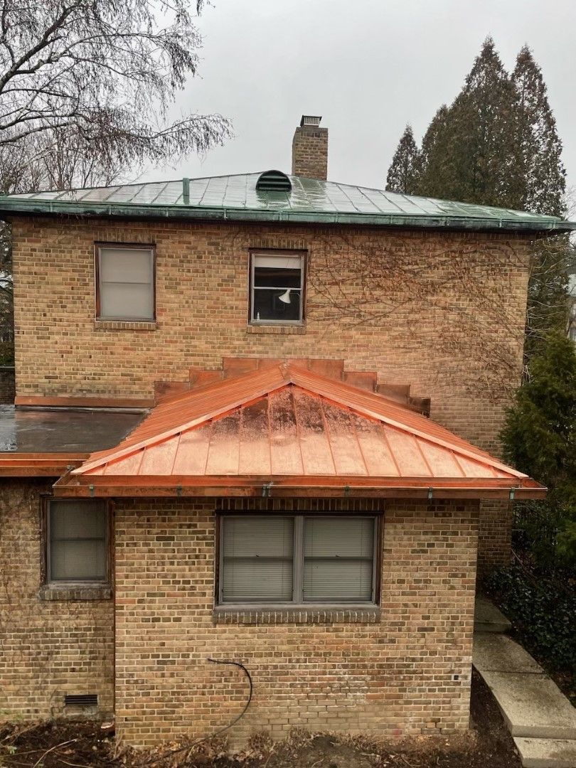 Two-story brick house with an orange metal roof over the front porch, seen from the street.