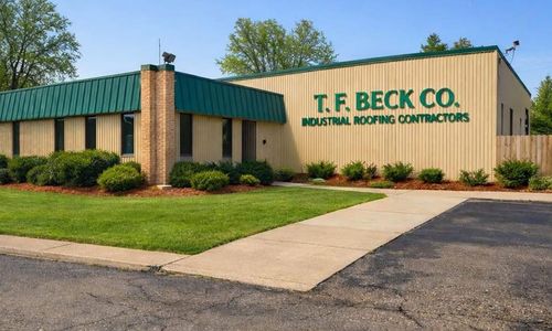 T.F. Beck Co. building with green roof and sign reading “Roofing Contractors” beside a lawn and sidewalk
