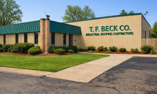 T.F. Beck Co. building with green roof and sign reading “Roofing Contractors” beside a lawn and sidewalk