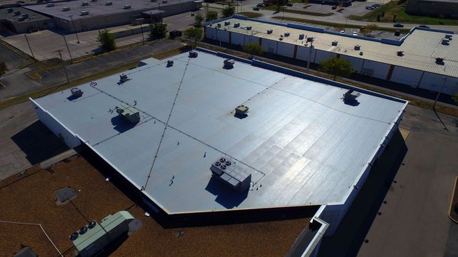 Aerial view of a large white commercial roof with vents and skylights in an industrial area