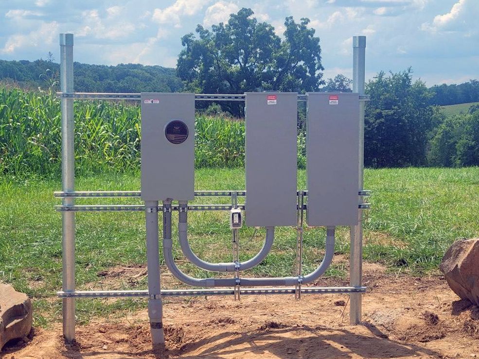 A fence with two electrical boxes in the middle of a field