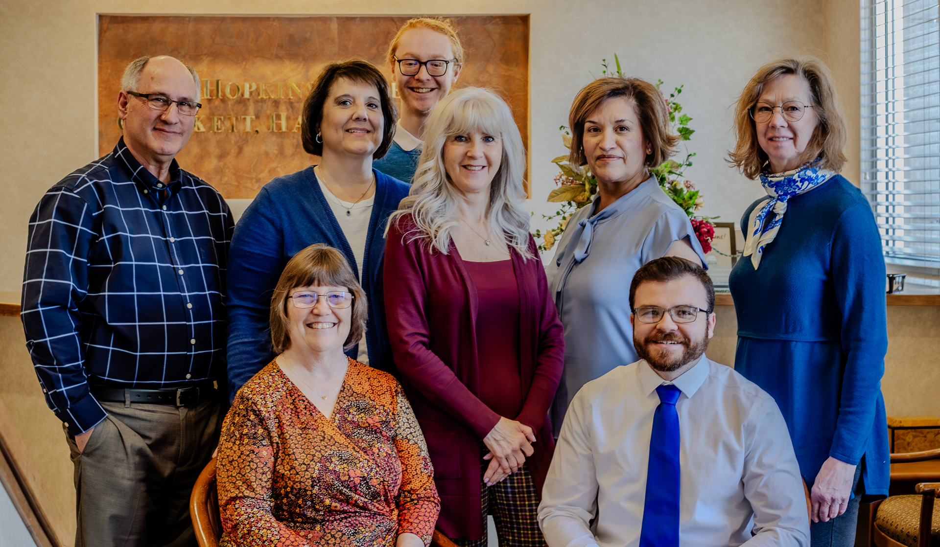Group of nine smiling people in an office setting, posing for a photo.
