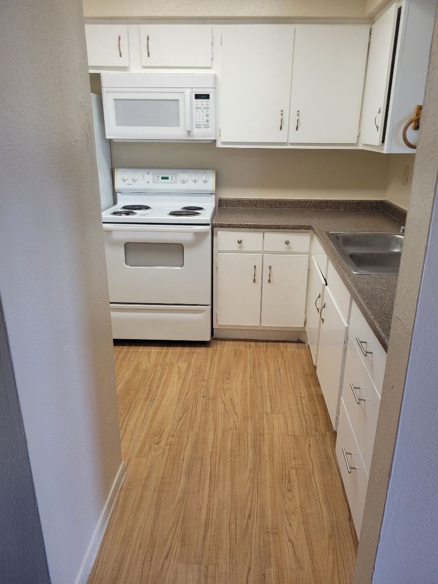 A kitchen with a stove, microwave, sink, and cabinets