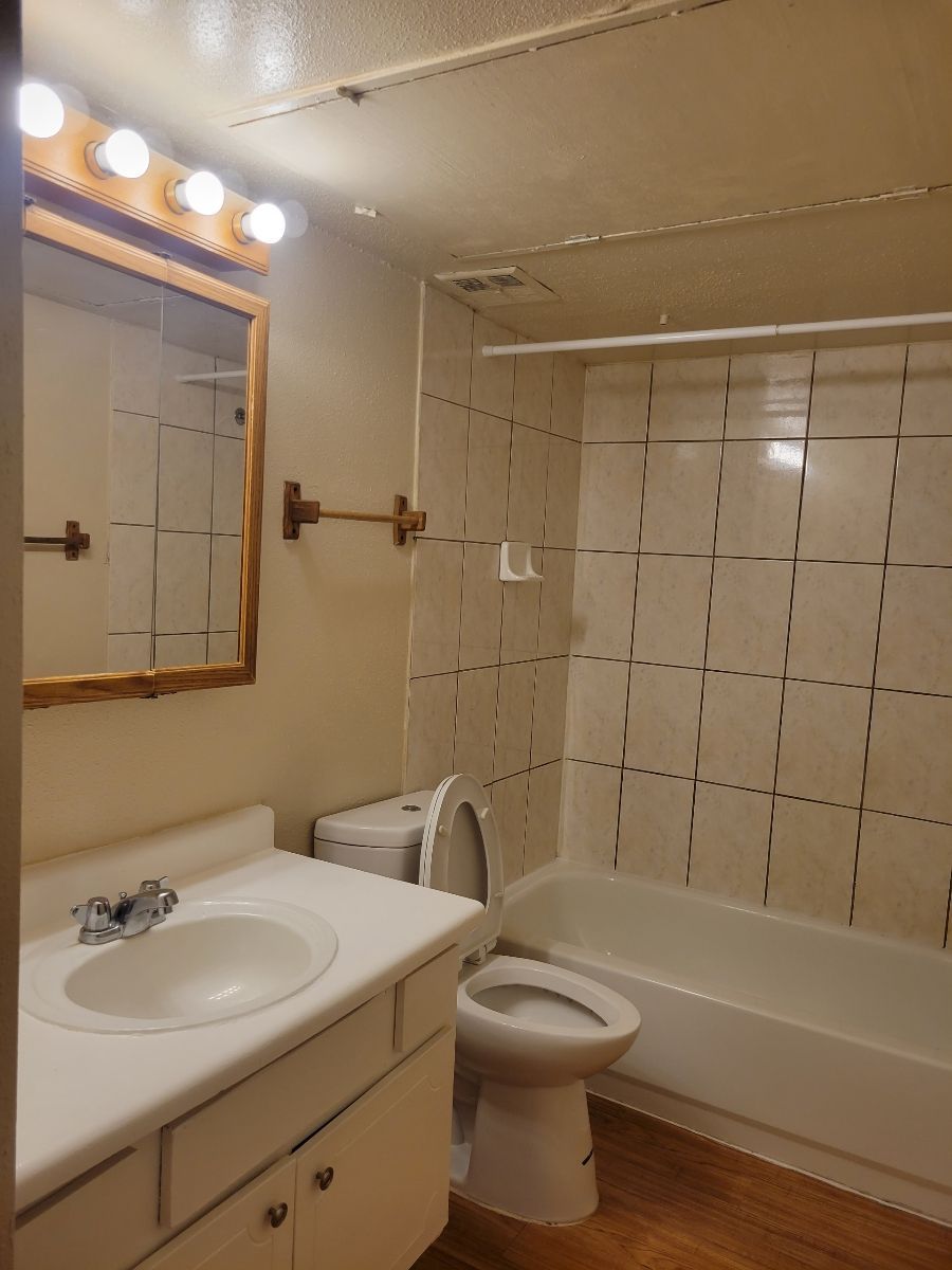 A bathroom with a tub, toilet, sink, and mirror