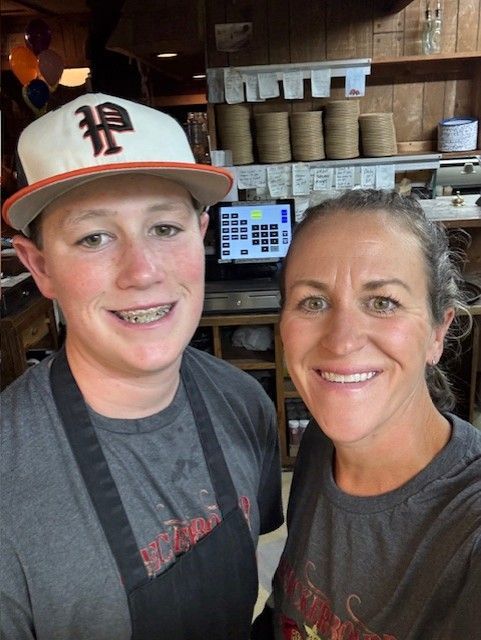 Two people smiling at the camera, one wearing a baseball cap and braces, the other in a t-shirt; they are likely at a restaurant.