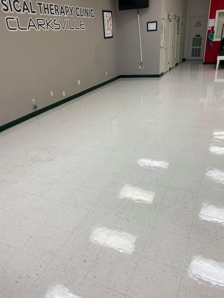 A large empty room with a white tile floor and a sign on the wall that says physical therapy clinic clarksville.