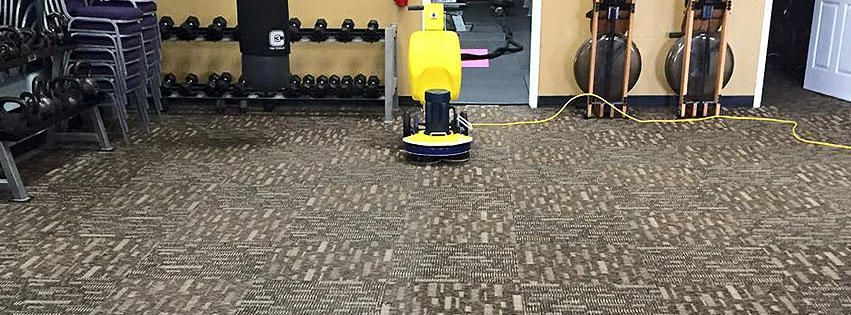 A yellow vacuum cleaner is sitting on a carpeted floor in a gym.