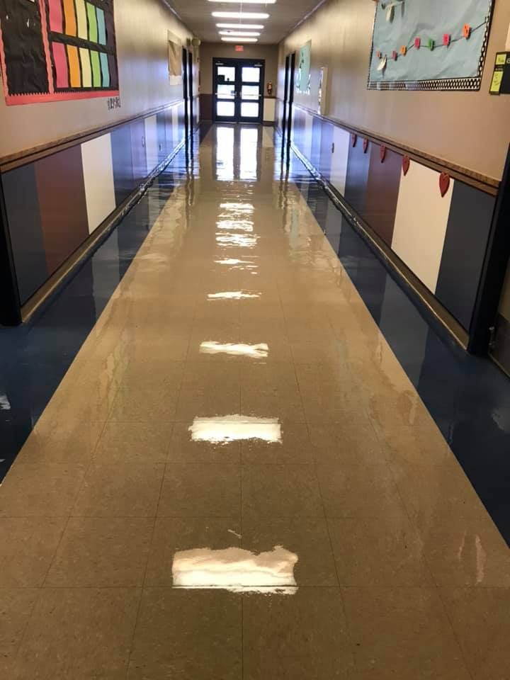 A long hallway in a school with a reflection of the lights on the floor.