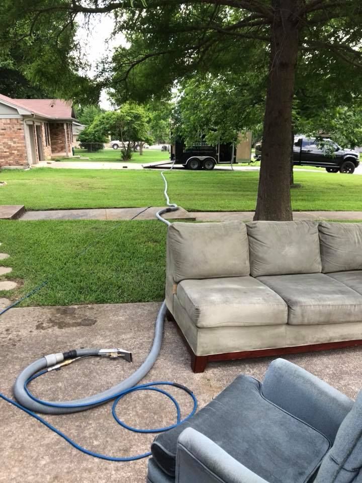 A couch is being cleaned outside with a vacuum cleaner.