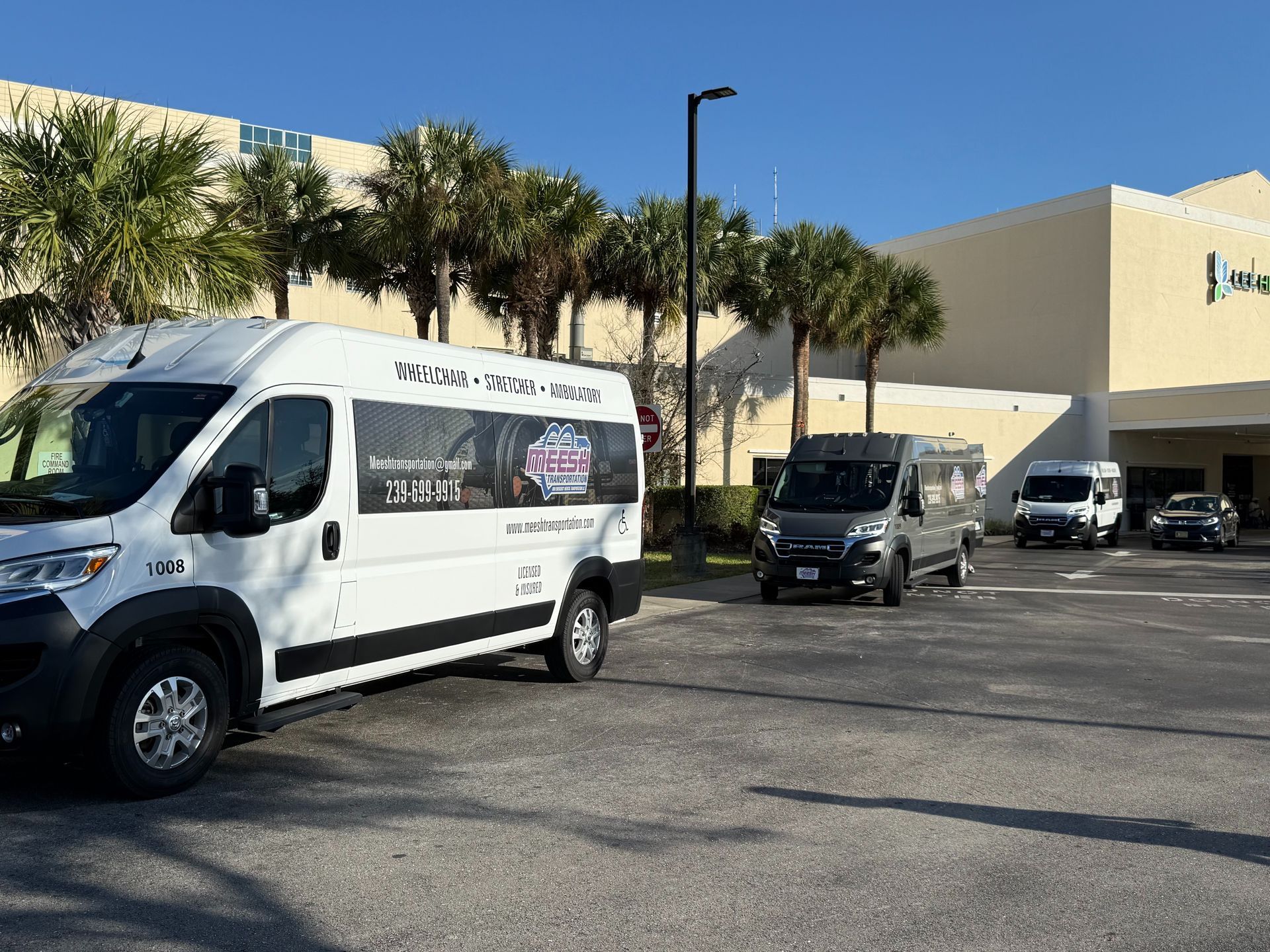 Three vans parked in a parking lot in front of a building with palm trees on a sunny day.