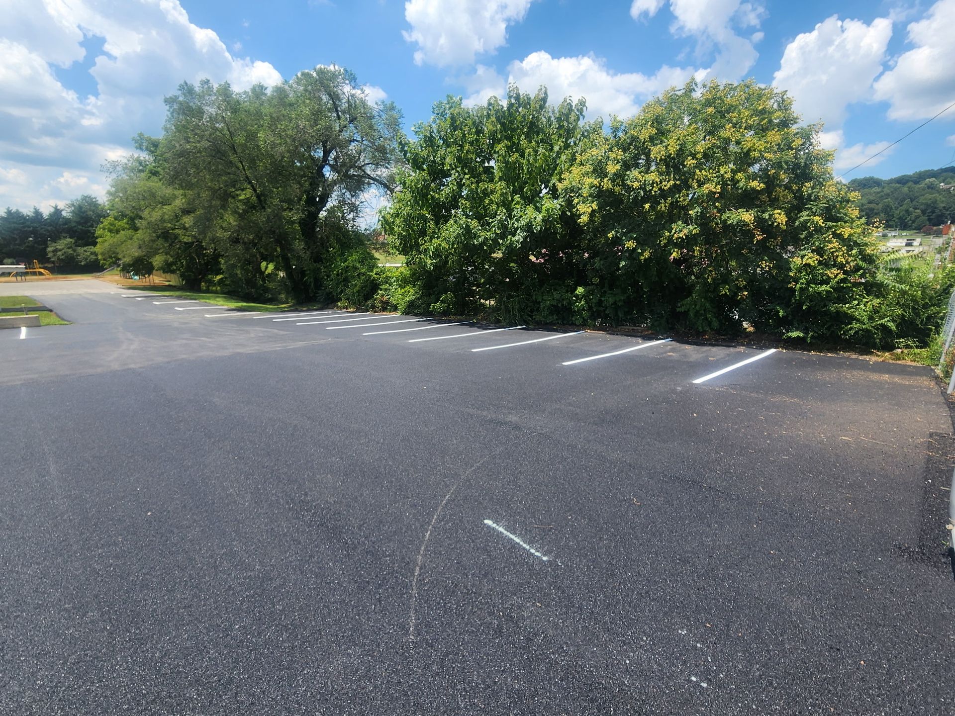 Paved parking lot with white parking space lines, trees and blue sky in the background.