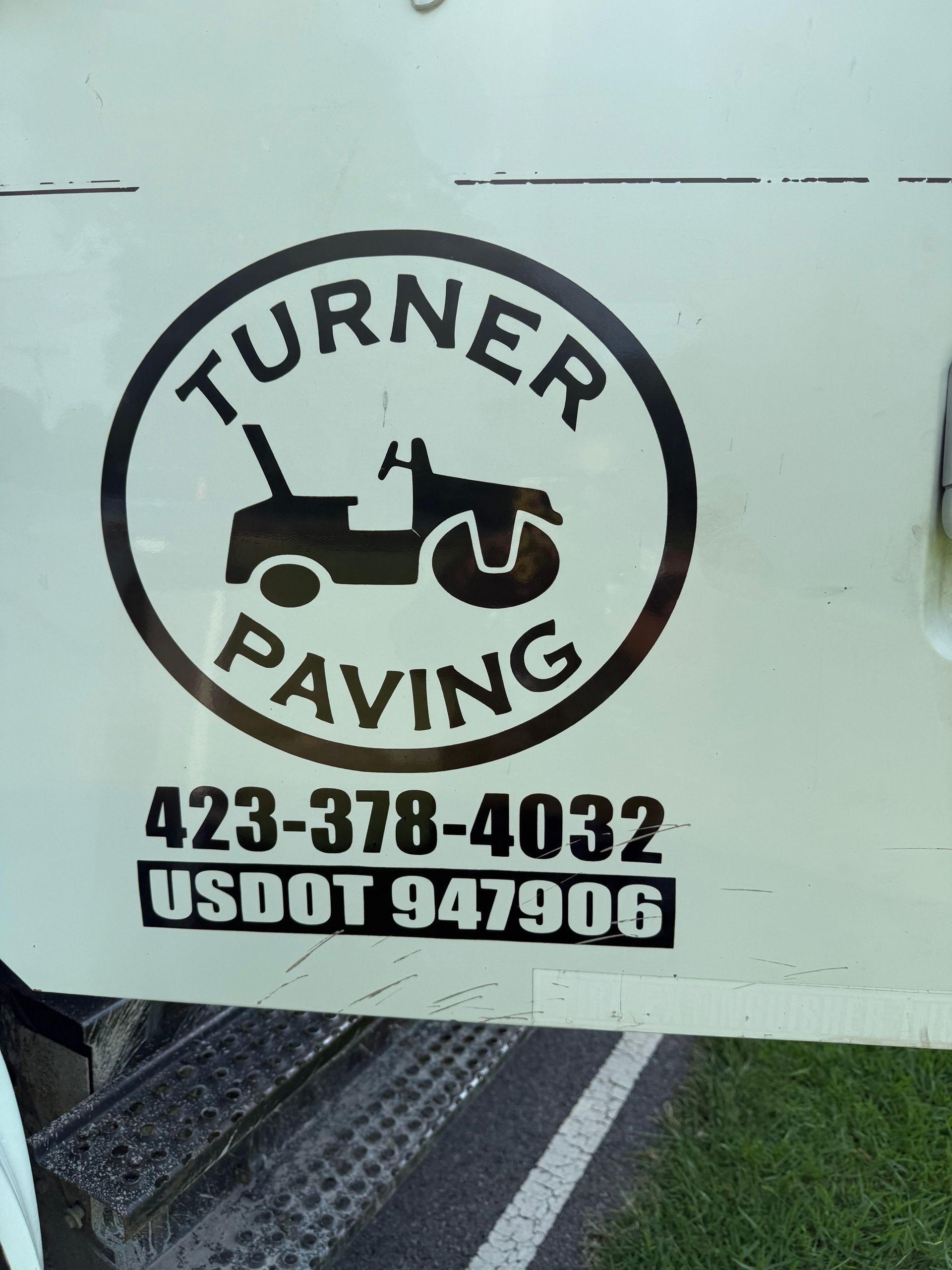 White truck with a black logo for Turner Paving: a roller and text within a circle, plus phone number and USDOT.