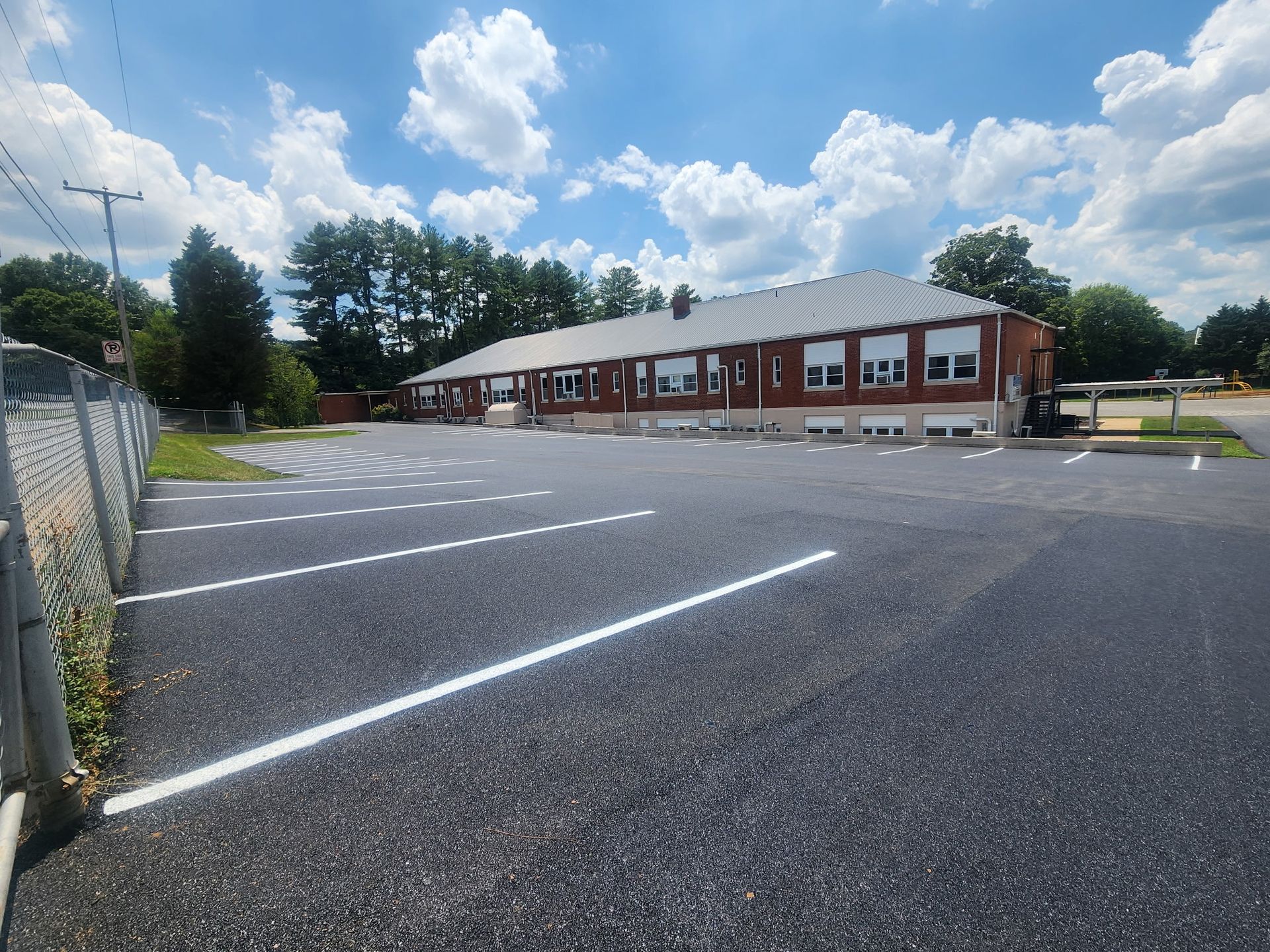 Exterior view of a one-story brick school building with a parking lot. Blue sky with clouds overhead.