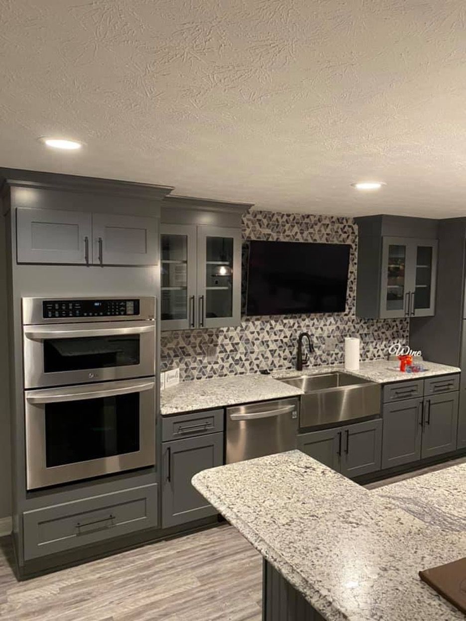 A basement kitchen with gray cabinets , stainless steel appliances , a sink , and a flat screen tv.