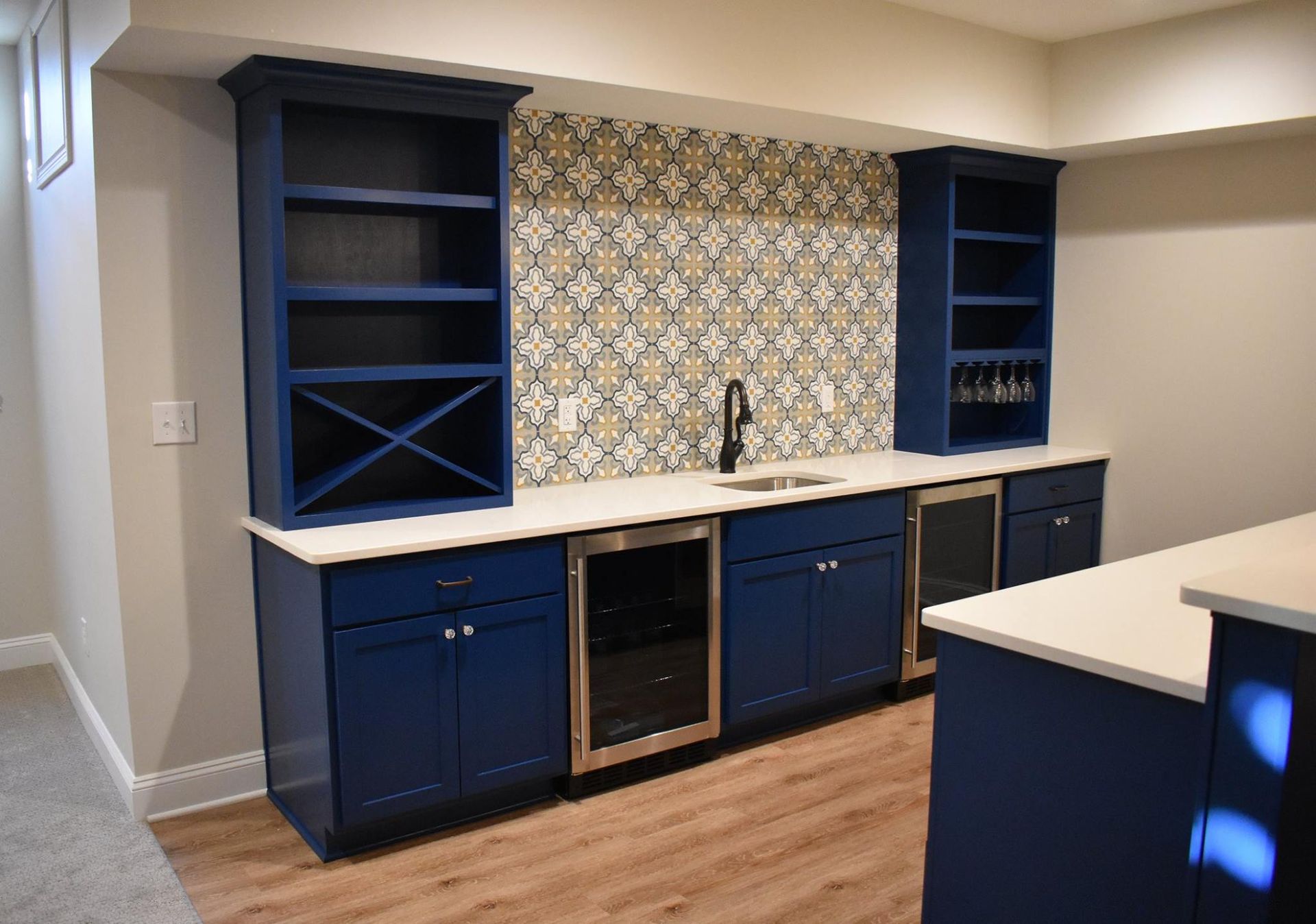 A finished basement kitchen with blue cabinets , stainless steel appliances , and a sink.
