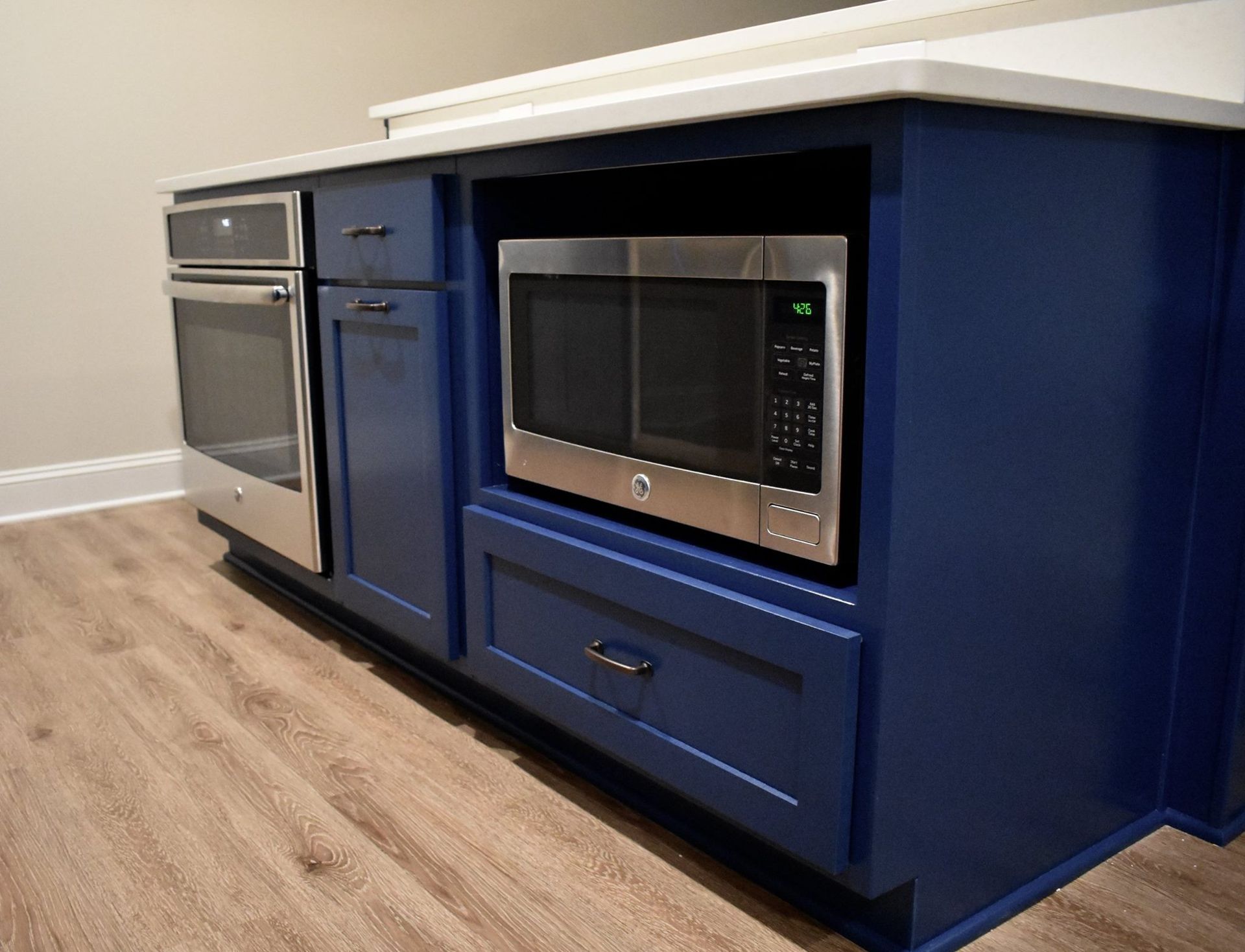 A basement kitchen with blue cabinets and a stainless steel microwave oven.