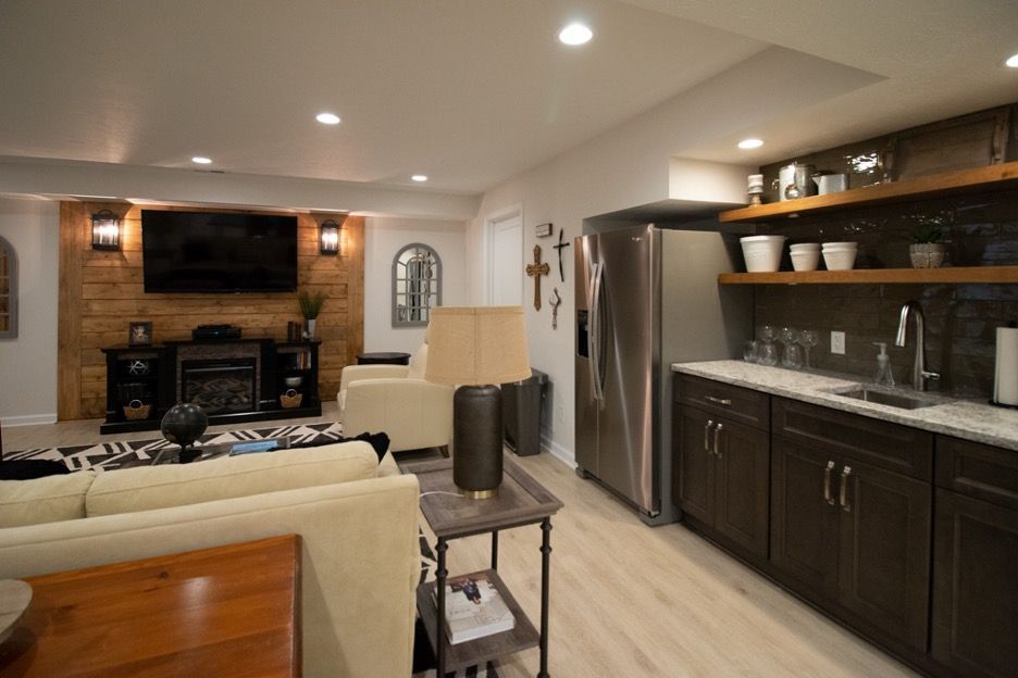 A basement living room with a couch , television , refrigerator and sink.