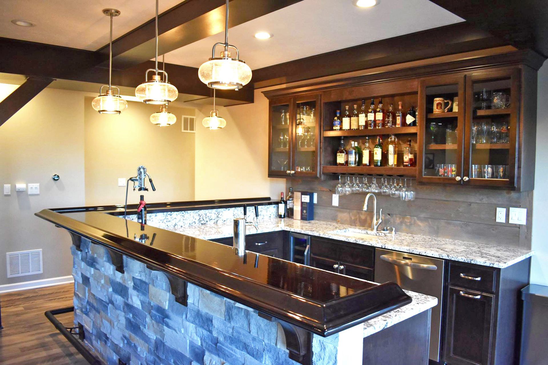 A basement kitchen with a bar and a lot of bottles on the shelves.
