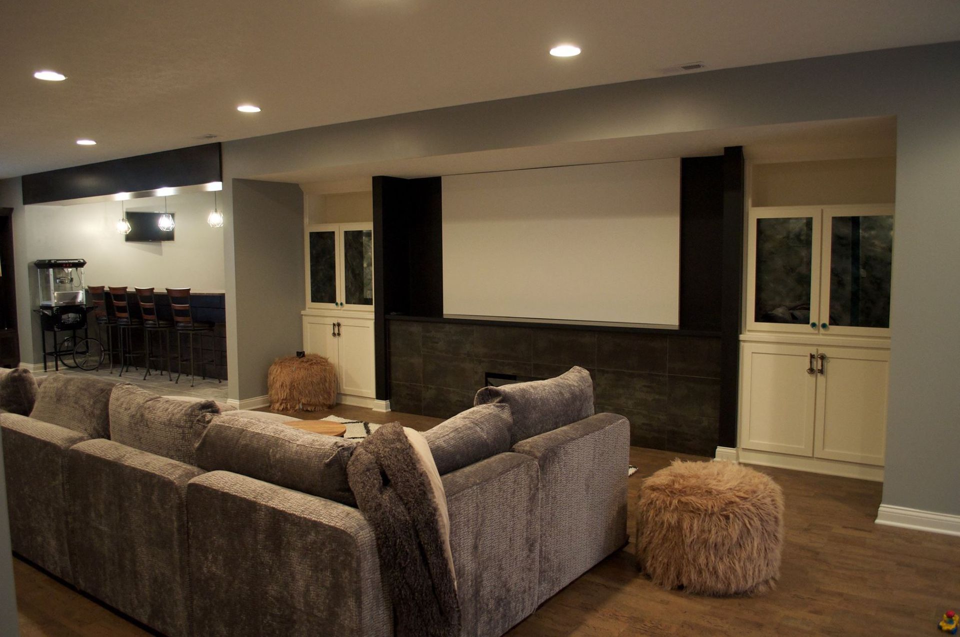A basement living room with a large couch and a projector screen.