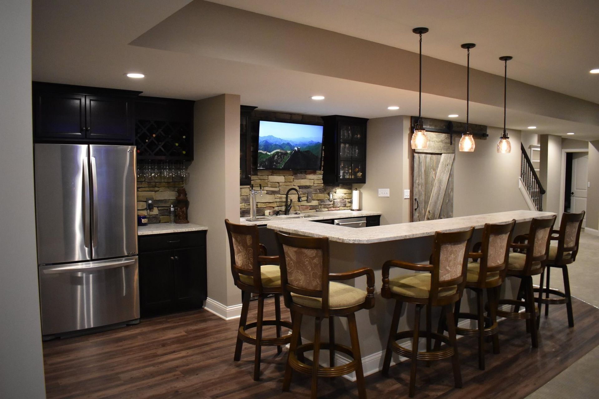 A basement with a bar , stools , a refrigerator and a television.