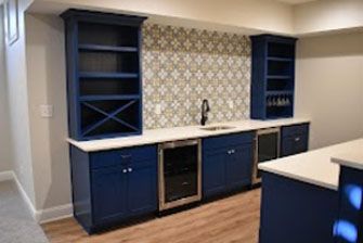 A navy blue home bar with white countertops, a decorative backsplash, and built-in shelving and appliances.