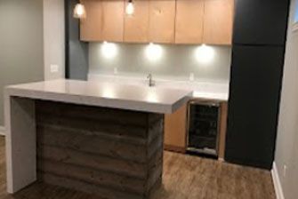 Basement bar with a wood and concrete island, light wood cabinets, and a black storage unit.