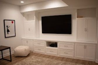 White built-in entertainment center with TV, storage cabinets, drawers, and art in a basement.