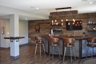 Basement bar with wooden accents, stools, and built-in shelving; a TV is mounted above the bar.