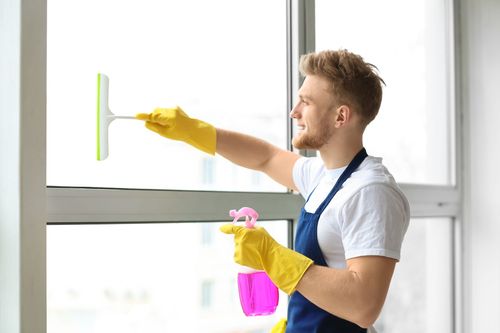 Man in gloves cleaning a window with a squeegee and pink spray bottle