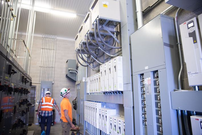 Two men are standing in a room with a lot of electrical equipment.