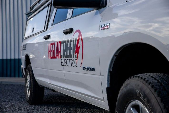 A white truck with the words Heglarcreek Electric on the side is parked in front of a building.