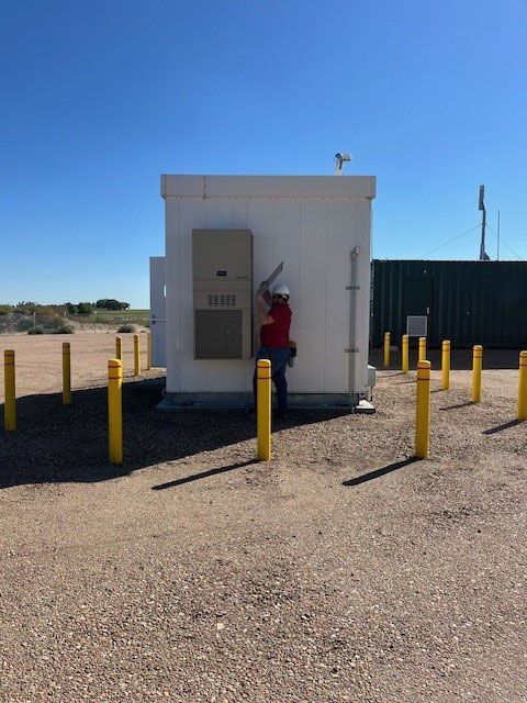 A man in a red shirt is standing in front of a small white building