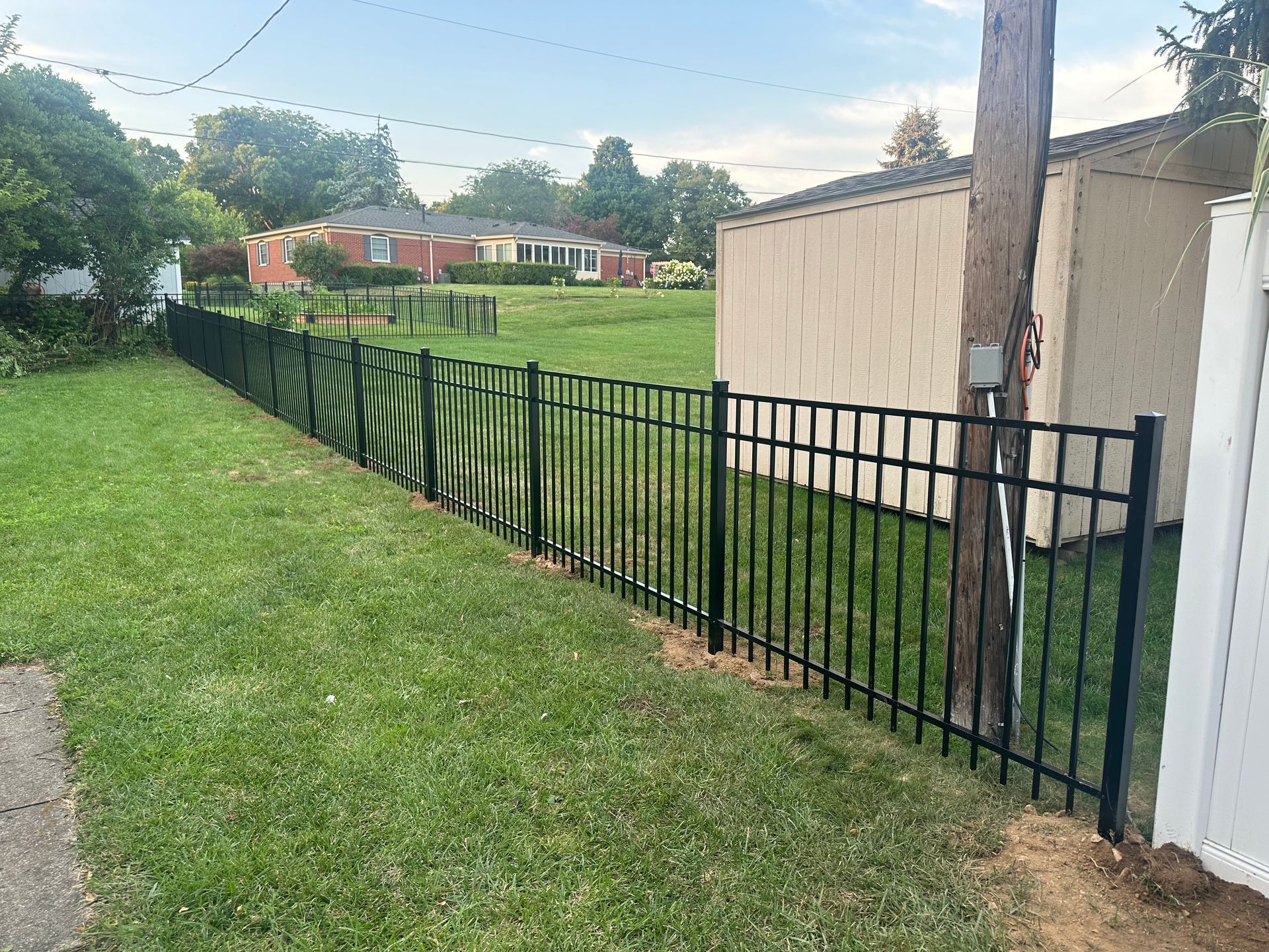 Black metal fence along a grassy yard, with a building and houses in the background.