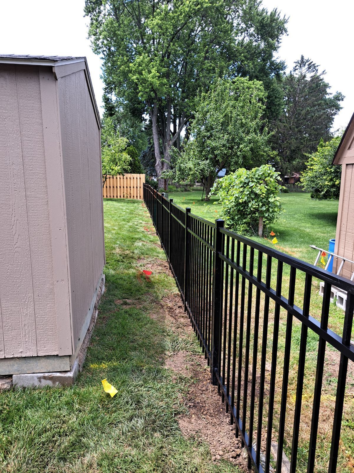 Black metal fence runs between two sheds on a grassy lawn.