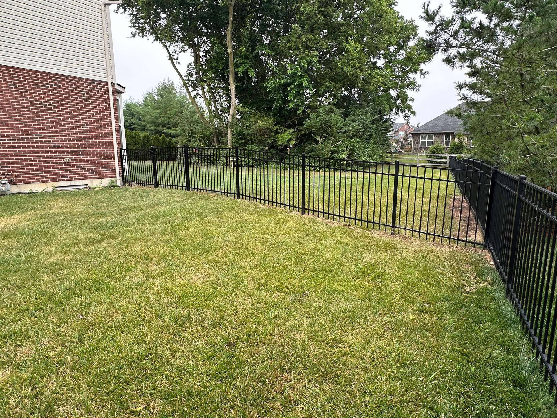 A black metal fence surrounds a green lawn in front of a brick building and trees.