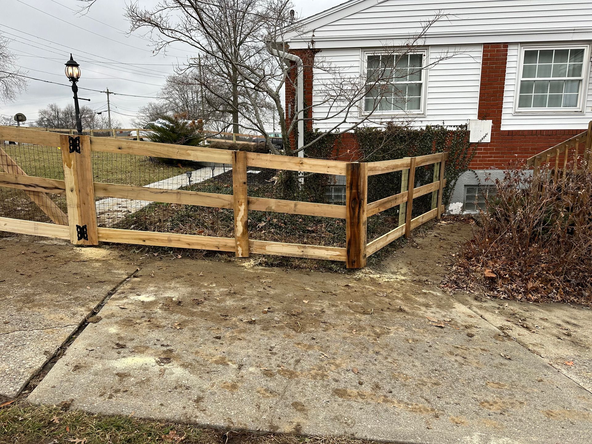 Wooden fence in front yard with a house and overcast sky in the background.