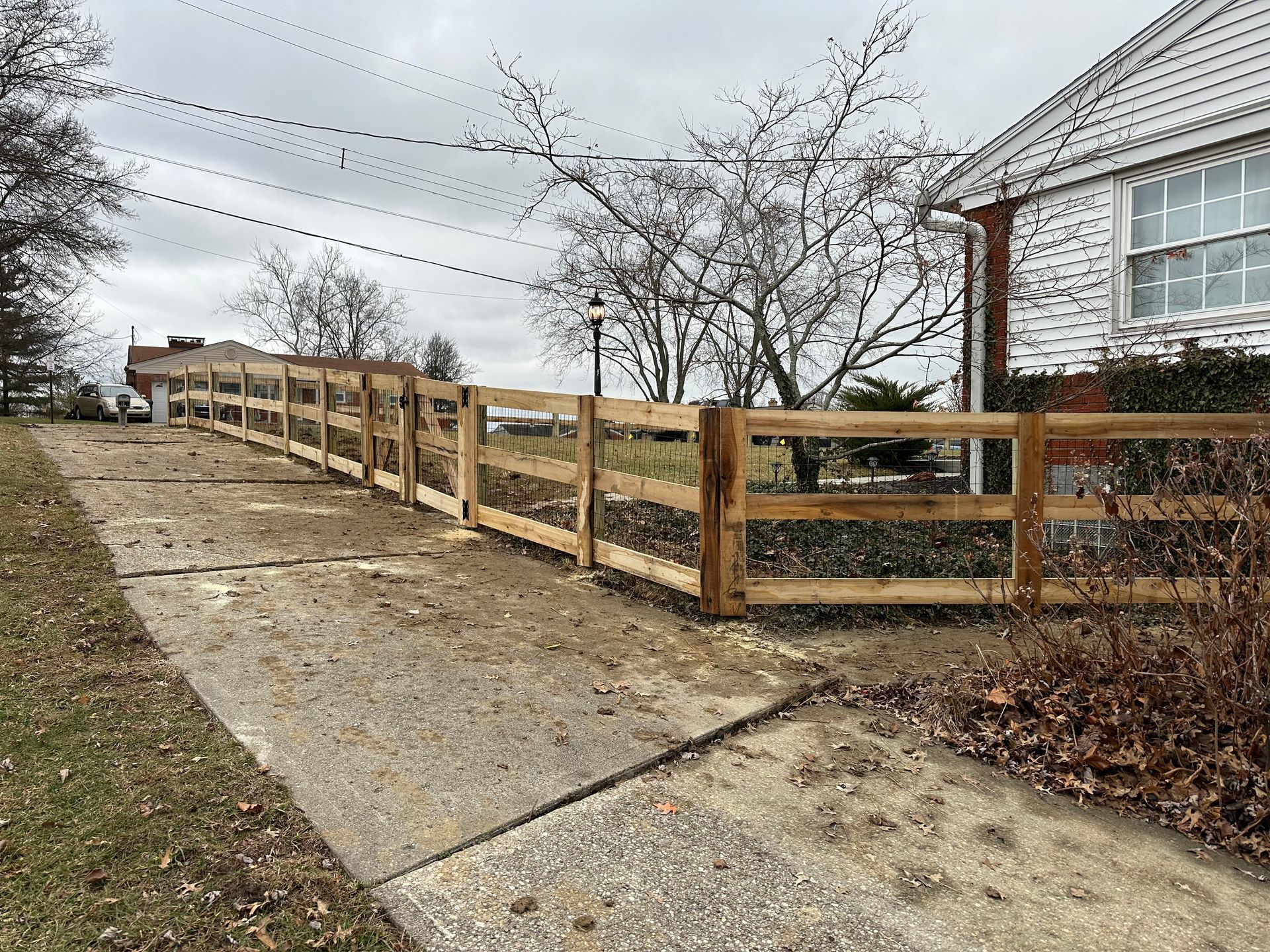 Wooden fence alongside a concrete driveway near a house. Overcast day.