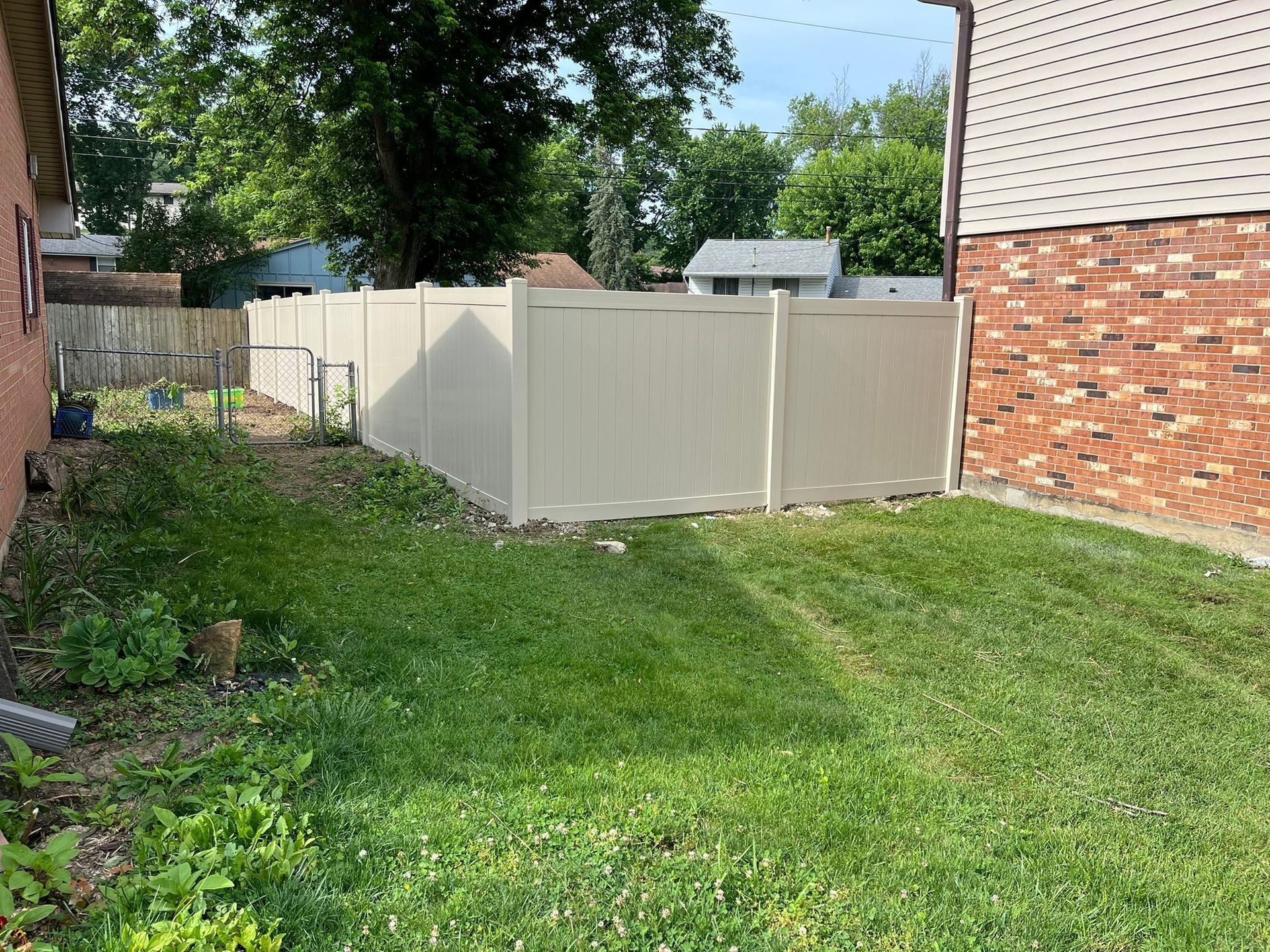 Tan vinyl fence in a grassy backyard, adjacent to a brick building.
