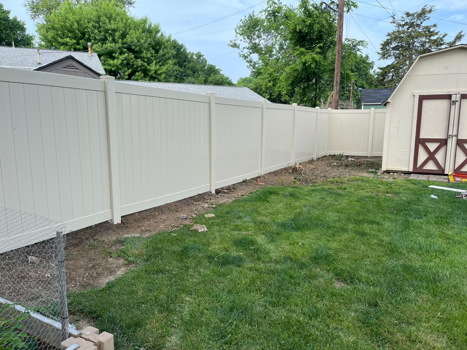 Beige vinyl fence in a backyard with green grass and a shed.